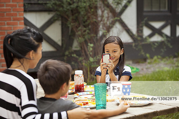Lächelndes Mädchen fotografiert Familie  während es am Picknicktisch sitzt