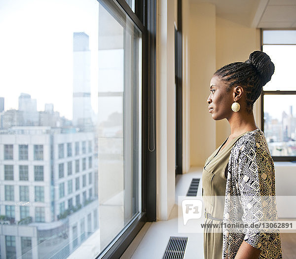 Seitenansicht einer nachdenklichen Geschäftsfrau  die im Büro am Fenster steht