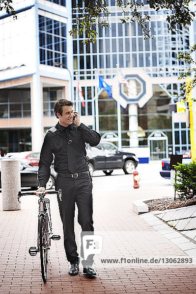 Geschäftsmann telefoniert  während er mit dem Fahrrad auf einem Fußweg in der Stadt unterwegs ist