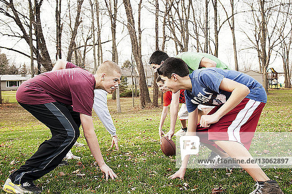 Smiling friends playing American football while bending over field in park
