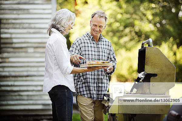 Happy senior couple preparing food while standing by barbecue grill in backyard