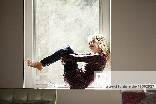 Seitenansicht einer lächelnden Frau  die zu Hause auf dem Fensterbrett sitzt