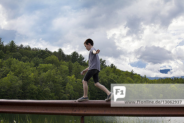 Seitenansicht eines Jungen  der auf einem Geländer vor bewölktem Himmel läuft