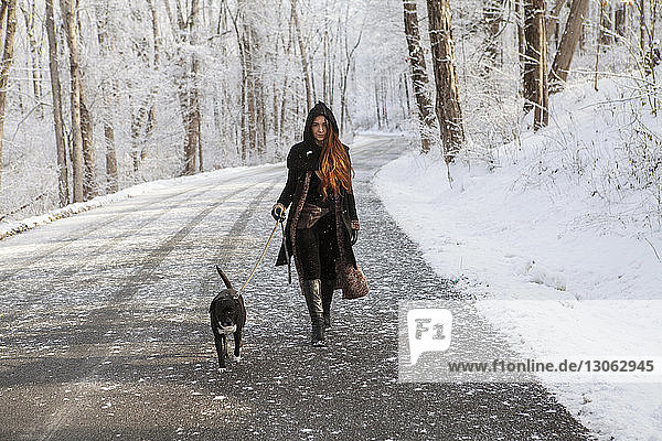 Porträt einer jungen Frau  die im Winter mit Hund auf der Strasse spazieren geht