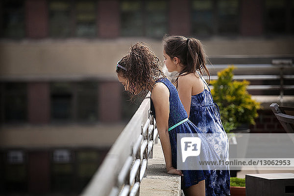Seitenansicht von Mädchen  die auf einem Geländer lehnen  während sie auf der Gebäudeterrasse stehen