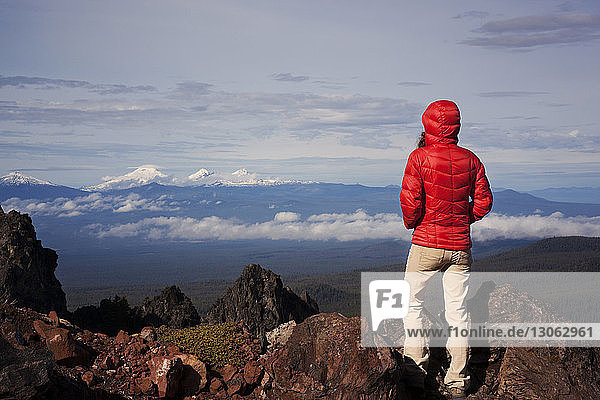 Rear view of woman wearing hooded shirt standing on mountain against sky