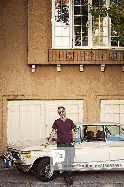 Porträt eines Mannes mit Sonnenbrille  der sich an ein Auto lehnt