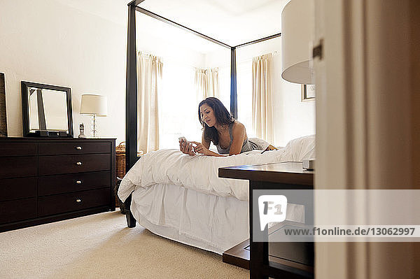 Happy woman using phone on bed in bedroom