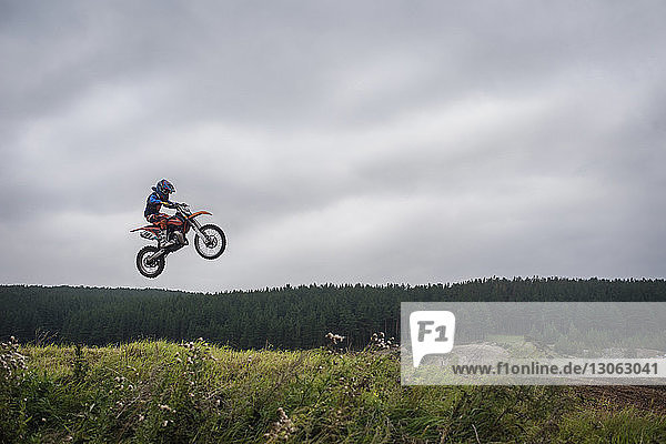 Biker performing stunt in mid-air against cloudy sky