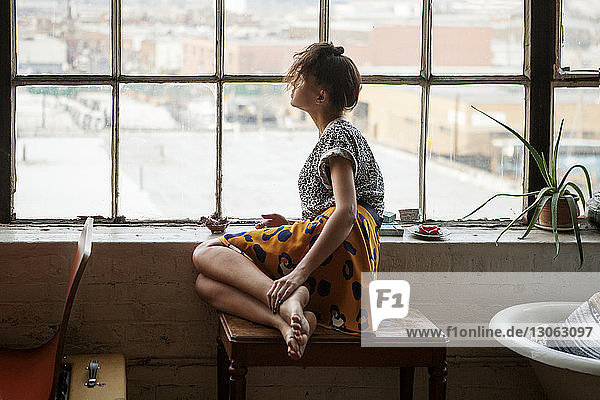 Woman looking through window while sitting on table at home