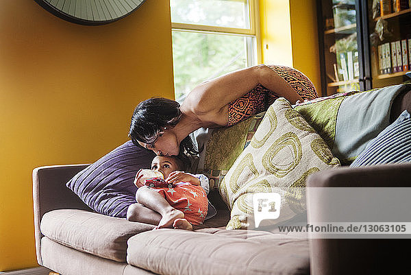 Mother kissing son lying on sofa at home
