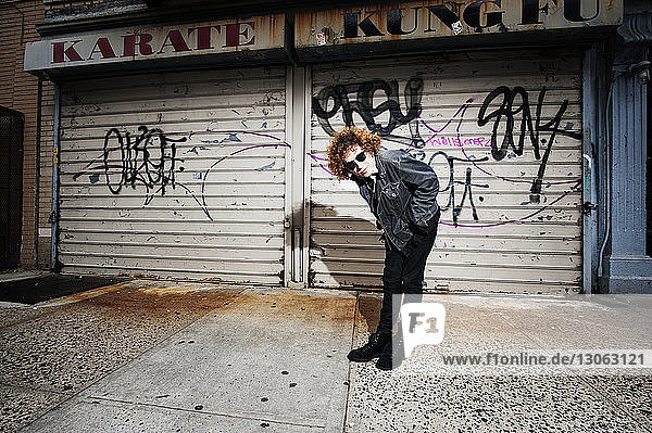 Porträt eines jungen Mannes  der sich auf einem Fußweg gegen Graffiti-Fensterläden beugt