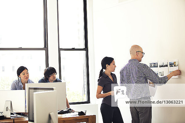 Geschäftsmann klebt Dokumente an die Wand  während er seinen Kollegen im Büro zur Seite steht