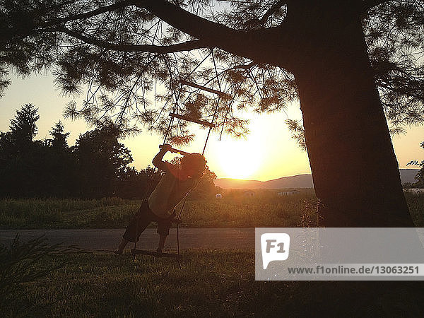 Rückansicht eines Jungen  der bei Sonnenuntergang auf eine Strickleiter auf dem Feld klettert