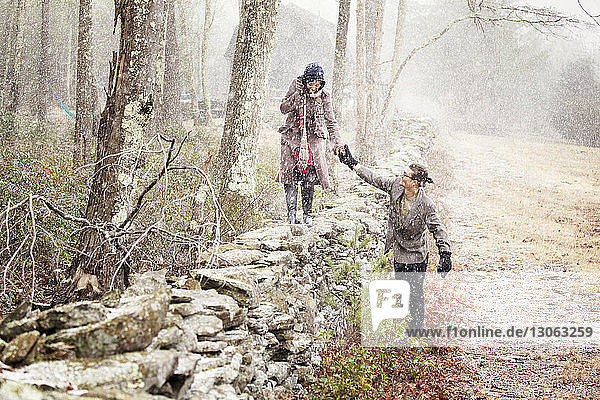 Man assisting woman walking on stone wall in winter