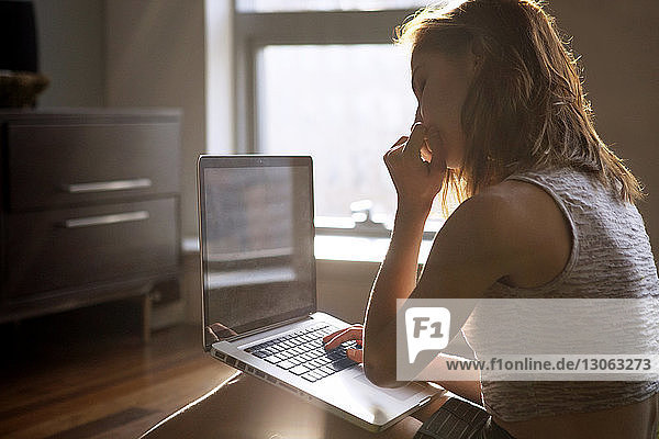 Nachdenkliche Frau benutzt Laptop  während sie zu Hause sitzt