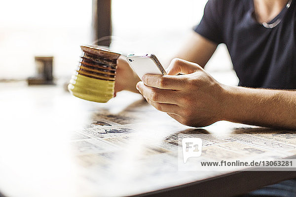 Ausgeschnittenes Bild eines Mannes  der ein Smartphone benutzt  während er Kaffee auf dem Tisch trinkt