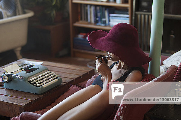 Frau trinkt Kaffee  während sie zu Hause an der Schreibmaschine sitzt