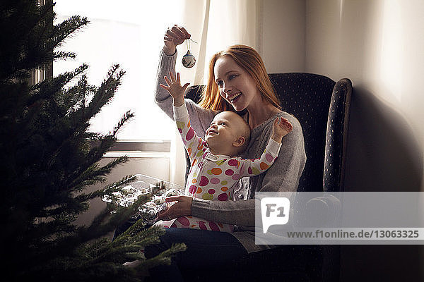 Mutter mit Tochter  die zu Hause auf einem Sessel sitzend den Weihnachtsschmuck ausbreitet