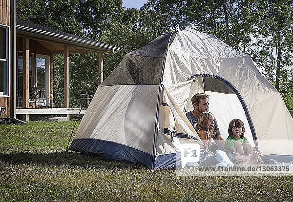 Kids with father looking away while sitting in tent