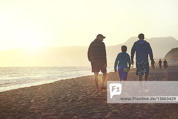 Rückansicht einer Familie  die bei Sonnenuntergang am Strand spazieren geht
