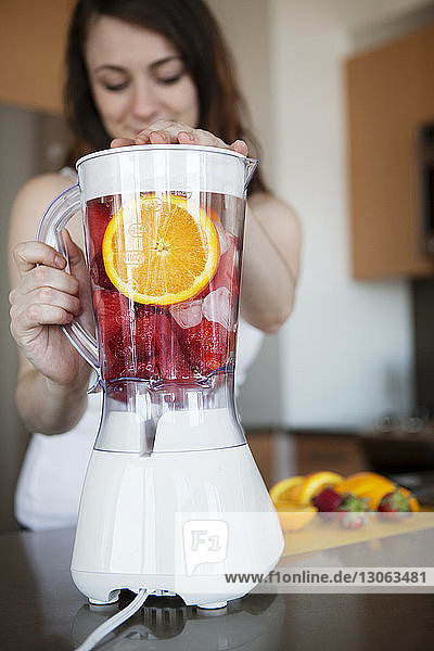 Woman preparing fruit juice in blender at home