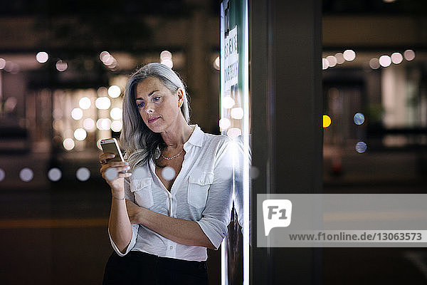 Geschäftsfrau telefoniert  während sie sich an ein Bushaltestellenplakat in der Stadt lehnt