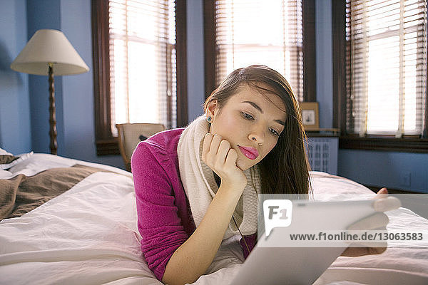 Woman using tablet computer while lying on bed at home