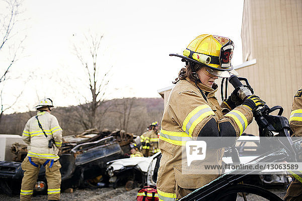 Weibliche Feuerwehrfrau schneidet Auto  während sie gegen den klaren Himmel steht