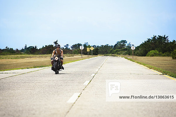 Mann fährt Motorrad auf Straße gegen klaren Himmel