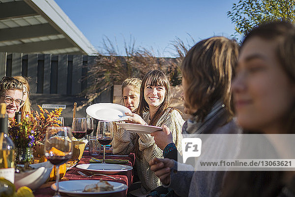 Happy woman passing plates to friends during garden party