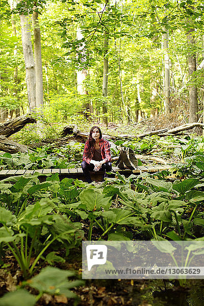 Frau schaut weg  während sie auf einem Steg im Wald sitzt