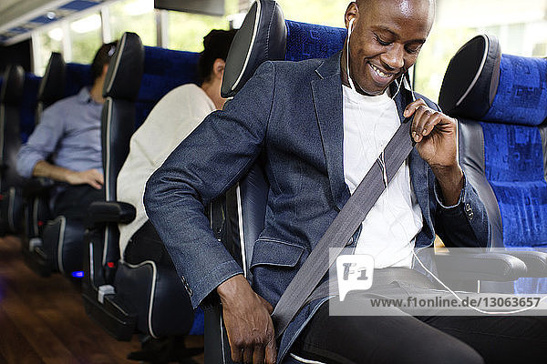 Happy man adjusting seat belt while sitting in bus