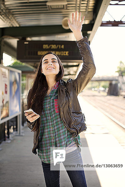 Lächelnde Frau winkt mit der Hand  während sie auf dem Bahnsteig steht