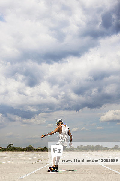 Rear view of man skateboarding on field against cloudy sky