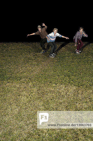 Niedriger Blickwinkel auf Freunde  die nachts auf einem Grasfeld Skateboard fahren