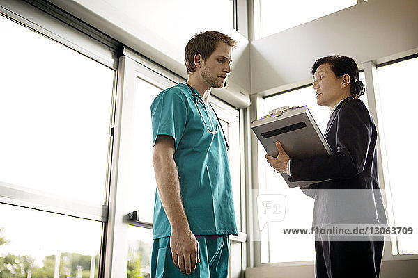 Businesswoman discussing document with doctor while standing in hospital