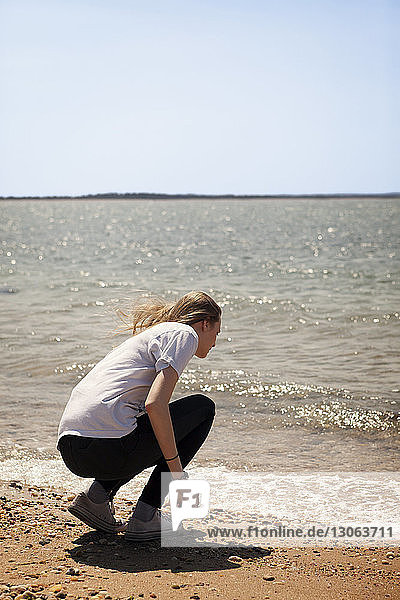 Rückansicht einer Frau  die am Strand am Ufer kauert