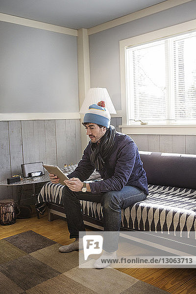 Mann benutzt Tablet-Computer  während er zu Hause auf dem Sofa sitzt