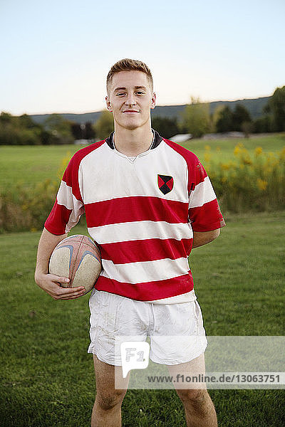 Portrait of confident player holding rugby ball on field against clear sky