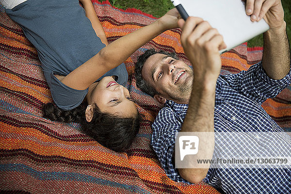 Happy father and daughter looking at tablet computer while lying on blanket in yard