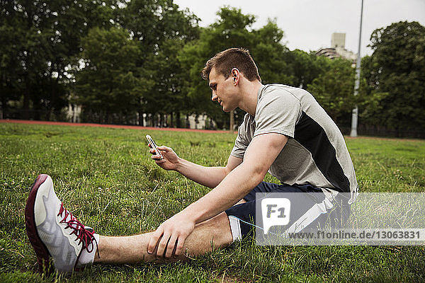 Mann benutzt Smartphone  während er im Park auf dem Feld sitzt