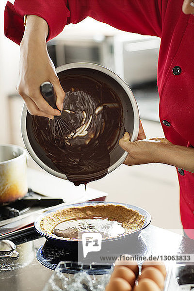 Mittelteil einer Frau  die geschmolzene Schokolade in einen Behälter gießt