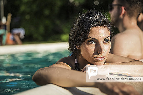 Nachdenkliche Frau schaut weg  während sie mit einem Freund im Pool steht