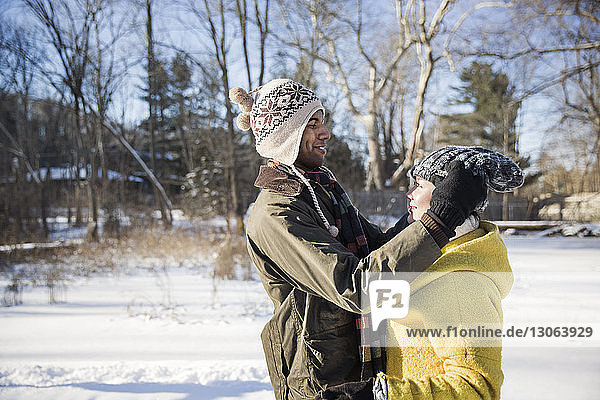 Seitenansicht eines Mannes  der eine Strickmütze zu einer Frau trägt  während er auf einem schneebedeckten Feld steht