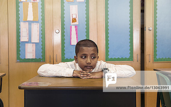 Gelangweilter Junge sitzt am Schreibtisch im Klassenzimmer