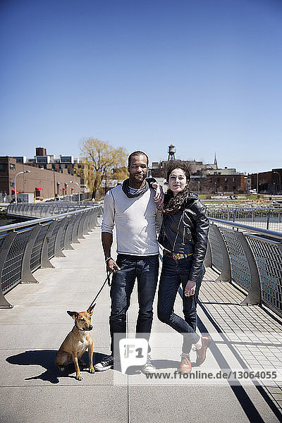 Portrait of happy couple with dog on footbridge against clear sky