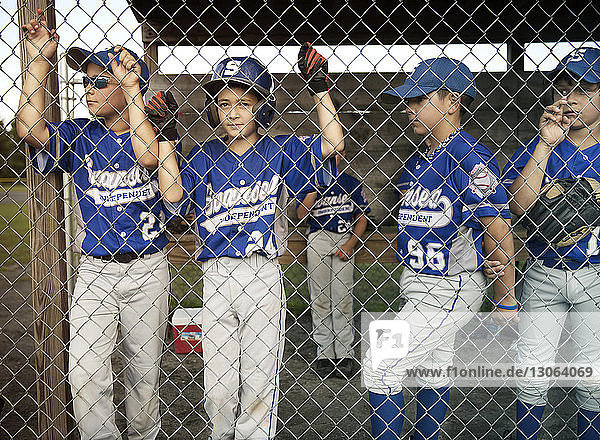 Portrait of boy with friends standing by fence in dugout