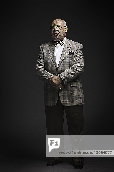 Senior man looking away while standing against black background