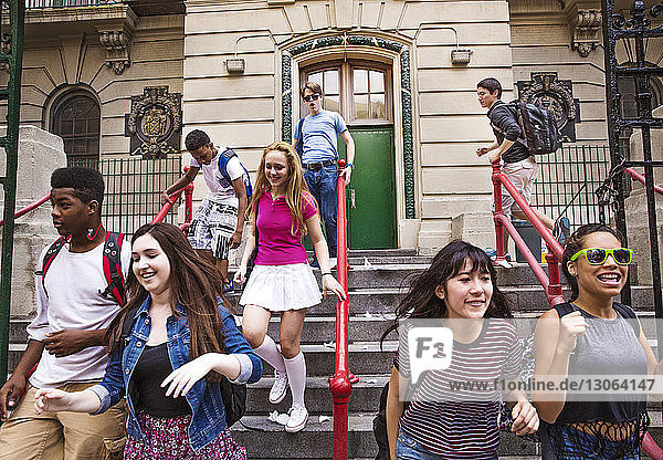 Glückliche Schülerinnen und Schüler bewegen sich auf Stufen vor der High School nach unten